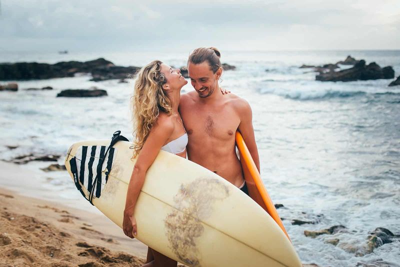 Ein glückliches Paar, das Surfbretter trägt und am Strand spazieren geht