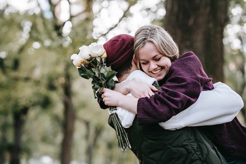 Lächelnde Frau umarmt ihren Freund und hält weiße Rosen in der Hand