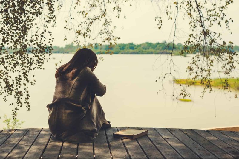 Eine traurige Frau sitzt auf dem Pier und blickt auf den See