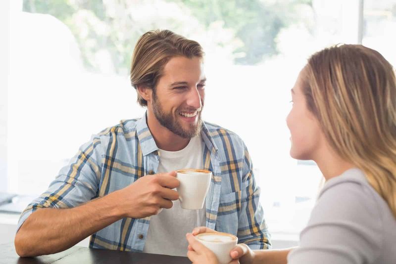 Ein lächelnder Mann, der mit einer Frau, die Kaffee trinkt, an einem Tisch sitzt