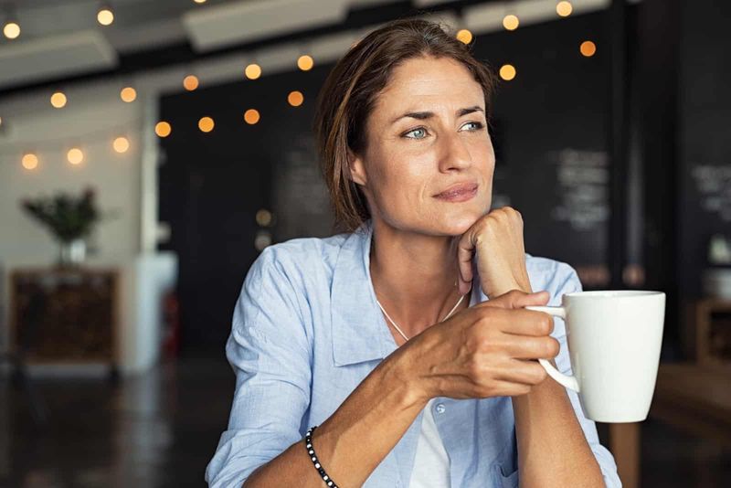 Reife Frau sitzt in der Cafeteria und hält eine Kaffeetasse in der Hand