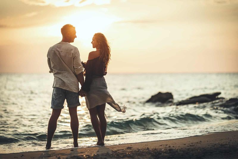 romantisches Paar bei Sonnenuntergang am Strand im Gespräch